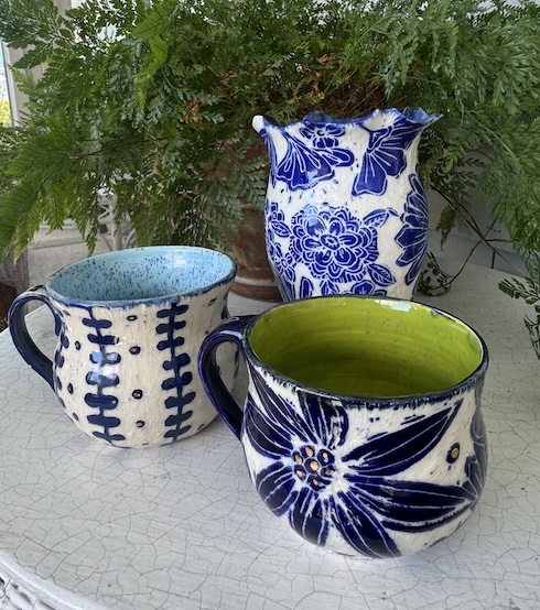 Two hand-decorated ceramic mugs and a floral pitcher made in pottery open studio class