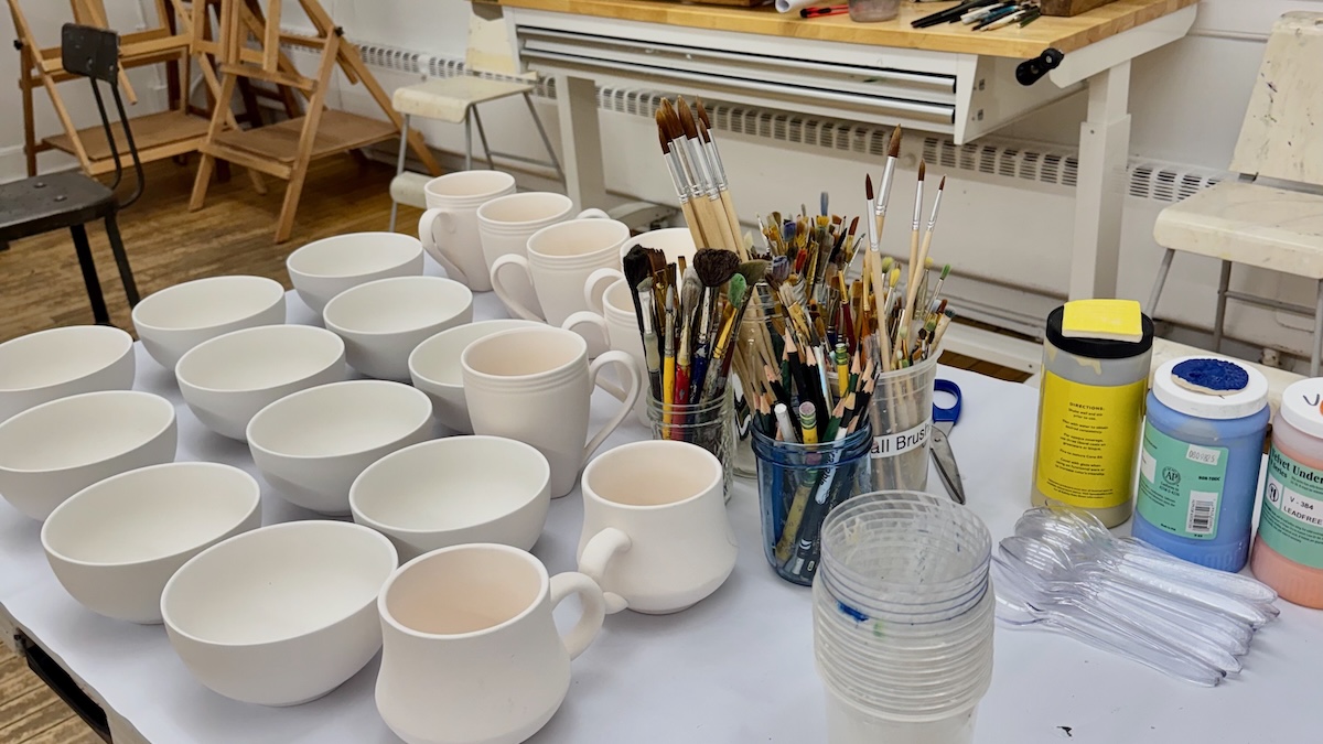 Ceramic mugs and bowls and pottery painting supplies set up for an Art Bar event at A Maker's Circle community art studio in Pottersville NJ