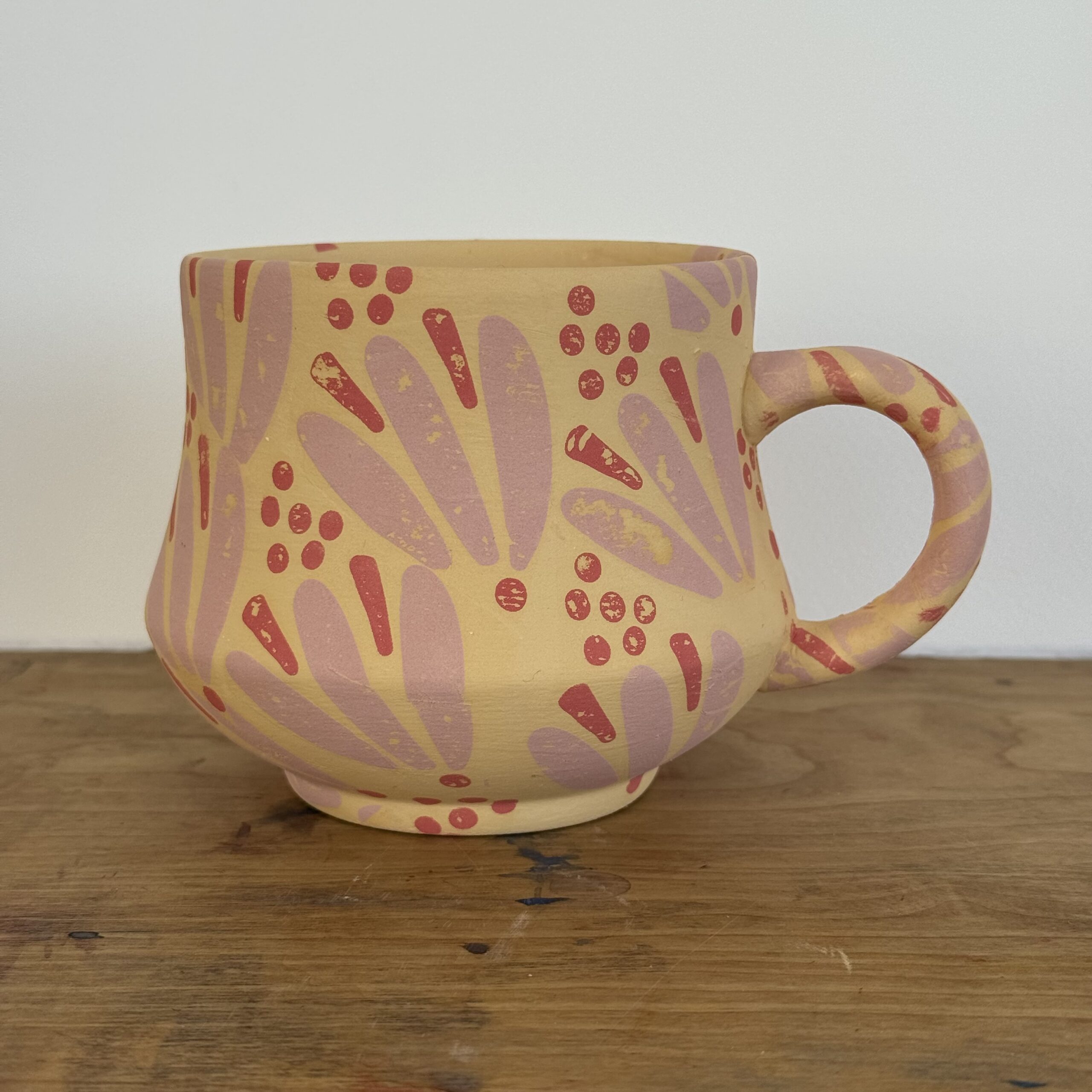 Hand-painted ceramic mug with a yellow base and pink floral petal design, an example of the Paint Your Own Pottery project at A Maker's Circle's Art Bar in Pottersville, NJ