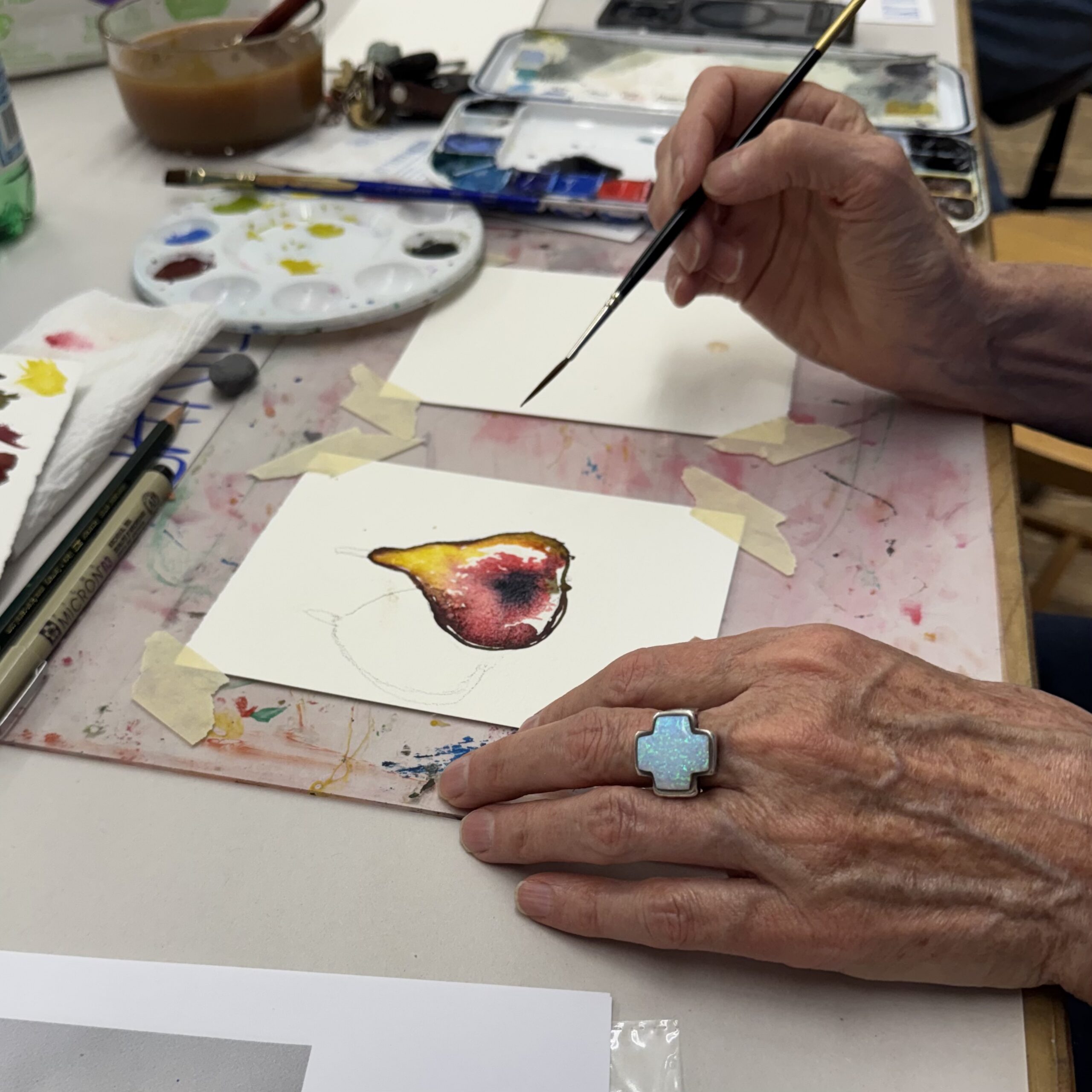 Close-up of hands painting a watercolor pear card at A Maker's Circle, part of the holiday wine and art night in Pottersville, NJ
