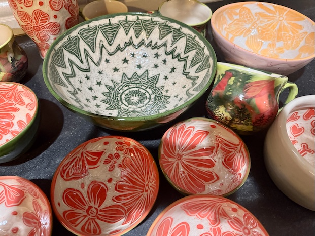 Ceramic bowls and mugs made by wheel throwing decorated with sgraffito floral and geometric patterns in red, green, and orange glazes