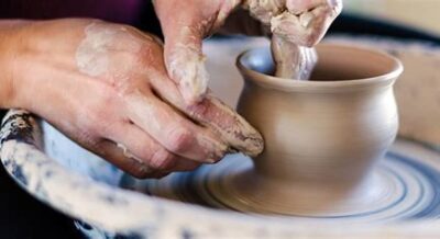 Hands shaping a clay pot on a pottery wheel in a one-time pottery wheel throwing class