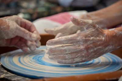 Instructor guiding student hands on clay during pottery wheel throwing class