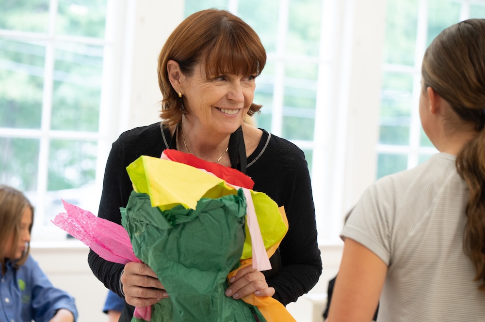 Jacqueline Pidgeon Pankuck, watercolor instructor at A Maker's Circle in Pottersville NJ, smiling while holding colorful tissue paper flowers in the art studio